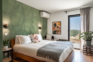 A bedroom with a bed, bedside tables, a potted plant, a painting, and a balcony with a view. - Ocean Breeze Retreat - Near Ericeira by Lisbeyond (Carvoeira)