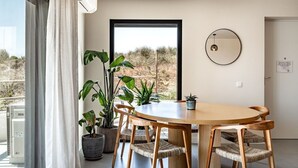 A dining area with a round table, six chairs, potted plants, a large window, and a door with a sign.
