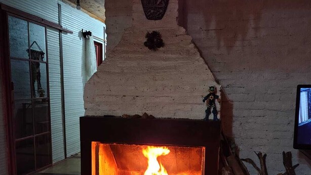 A fireplace with a fire, a book, a mug, and a small plant on a table.
