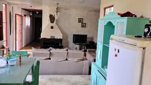 A living room with a sofa, a dining table with chairs, a television, and a refrigerator.