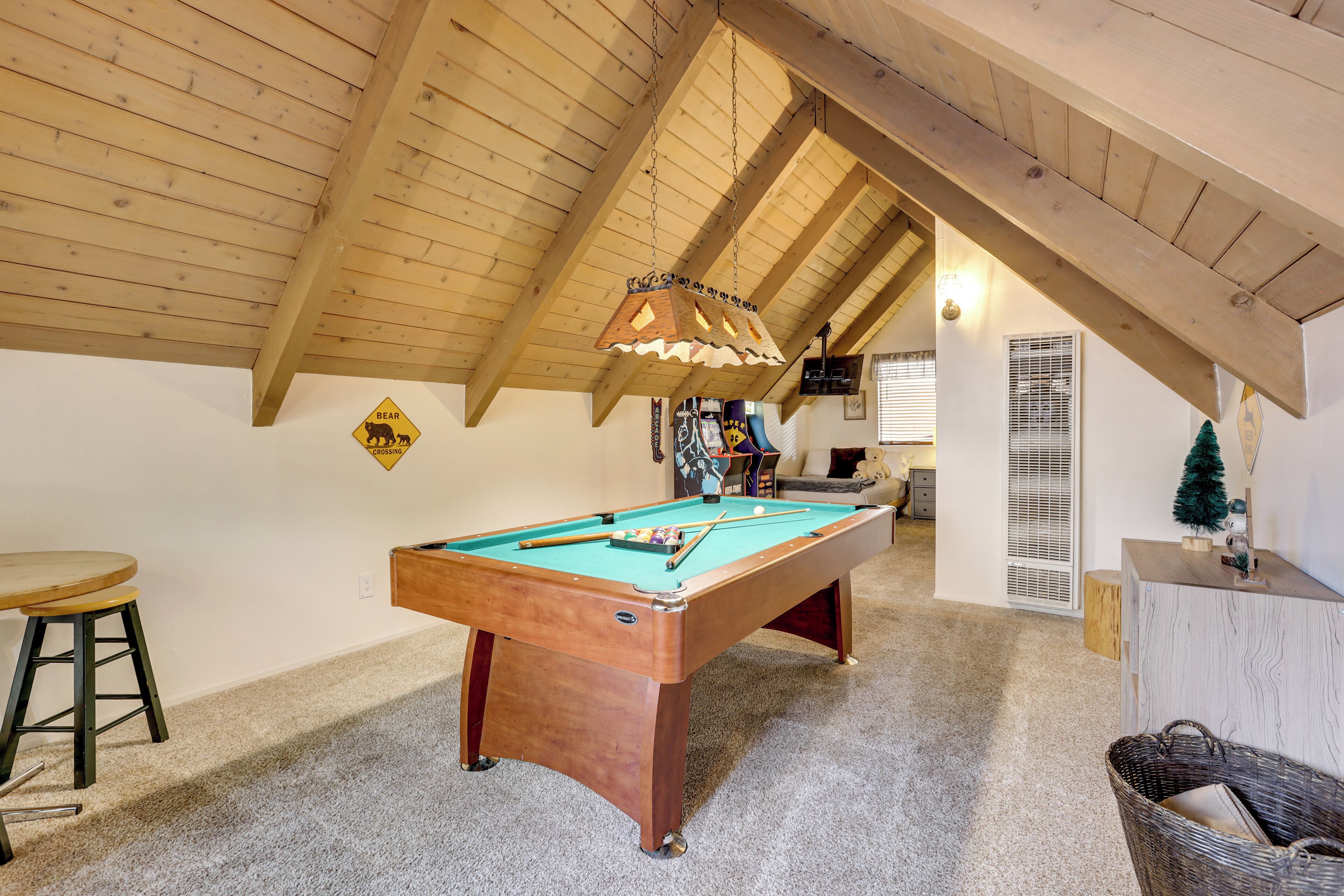 A pool table in a room with wooden beams on the ceiling, a bear warning sign, and a small Christmas tree.