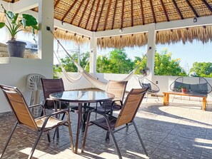 A covered outdoor seating area with a table and chairs, a hammock, and a fan.