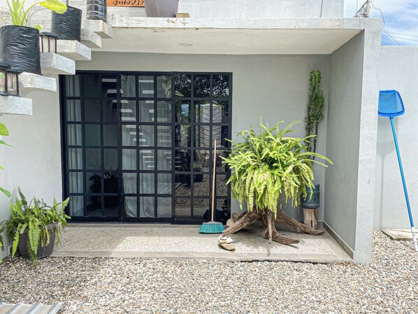 A modern building with a black door, a large potted fern, and a blue broom leaning against the wall.