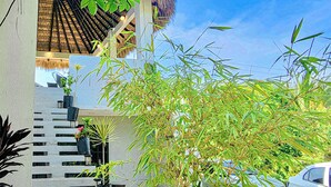 A modern building with a thatched roof, bamboo plants, and a car parked in front.