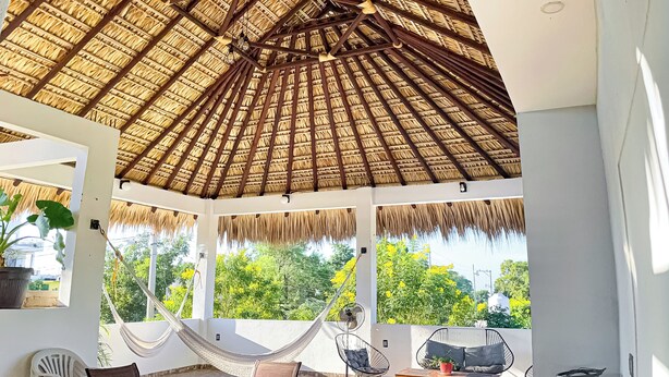 A covered outdoor seating area with a thatched roof, a round table, and chairs.