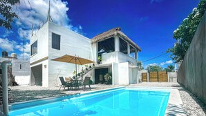 A modern house with a swimming pool, outdoor furniture, and a thatched-roof structure.