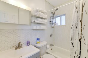 Een badkamer met een wit wastafel, toilet en bad. Boven het toilet bevindt zich een handdoekhouder en aan de muur een douchekop.