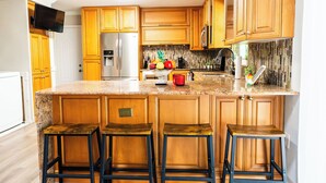 A kitchen with wooden cabinets, a stainless steel refrigerator, a granite countertop, and a built-in microwave.