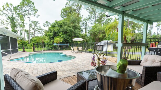 A covered outdoor area with a pool, wicker furniture, and a grill.