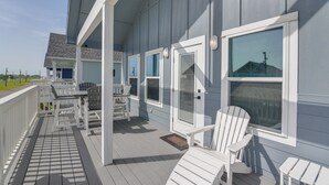 A covered outdoor deck with white Adirondack chairs, a table, and a door with a window.