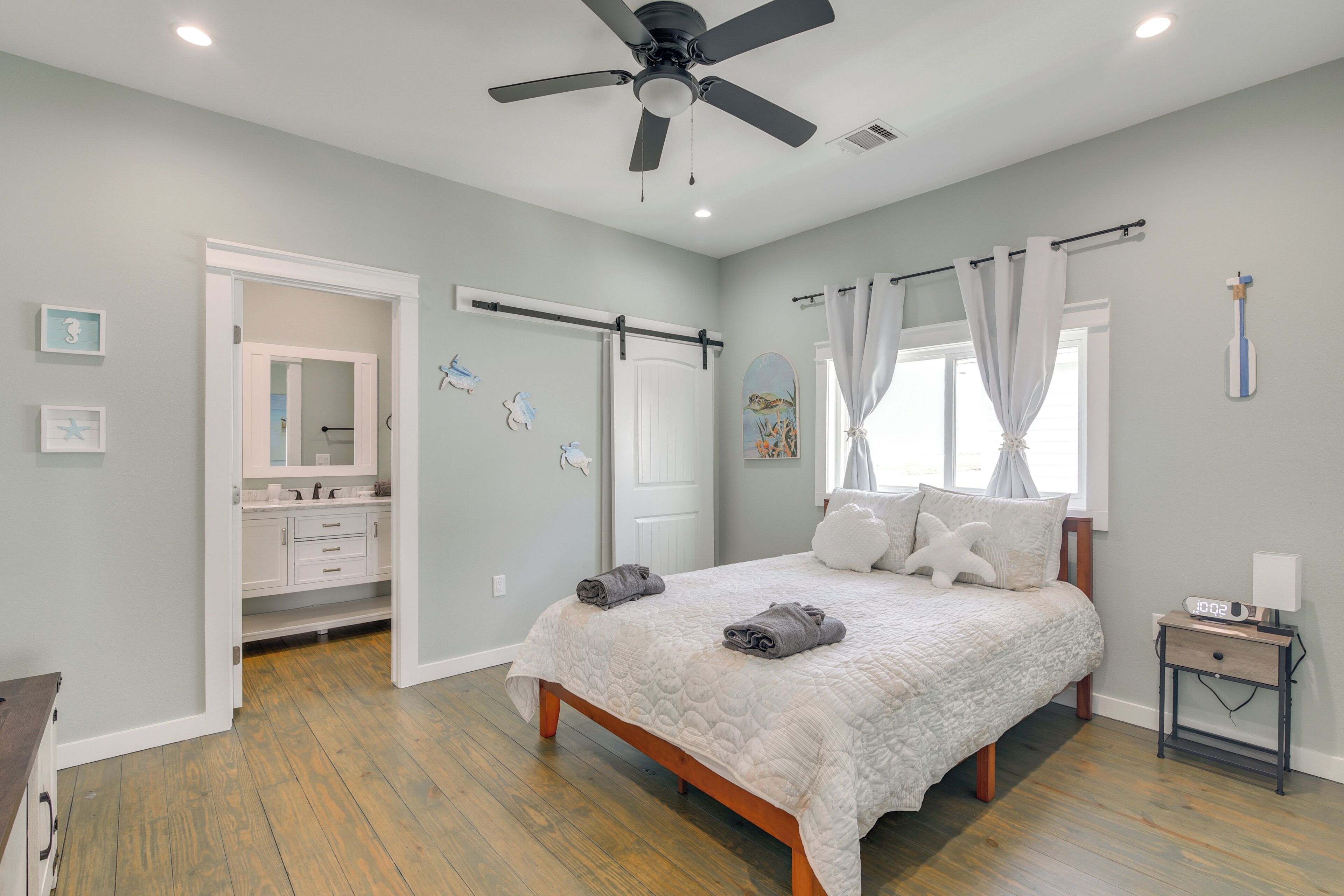 Ein Schlafzimmer mit Bett, Deckenventilator, Nachttisch und einem Fenster mit Vorhängen.