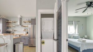 A compact living space with a kitchenette, a washing machine, and a bedroom with a bed and curtains.