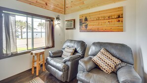 Een kamer met twee leren fauteuils, een houten krukje, een landschapsschilderij en een raam met gordijnen.