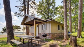 Een chalet met een picknicktafel en barbecue, omgeven door bomen en uitzicht op een meer.