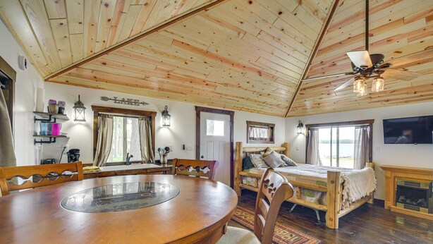 Een kamer met houten vloer, een ronde eettafel, een bed en een open haard.