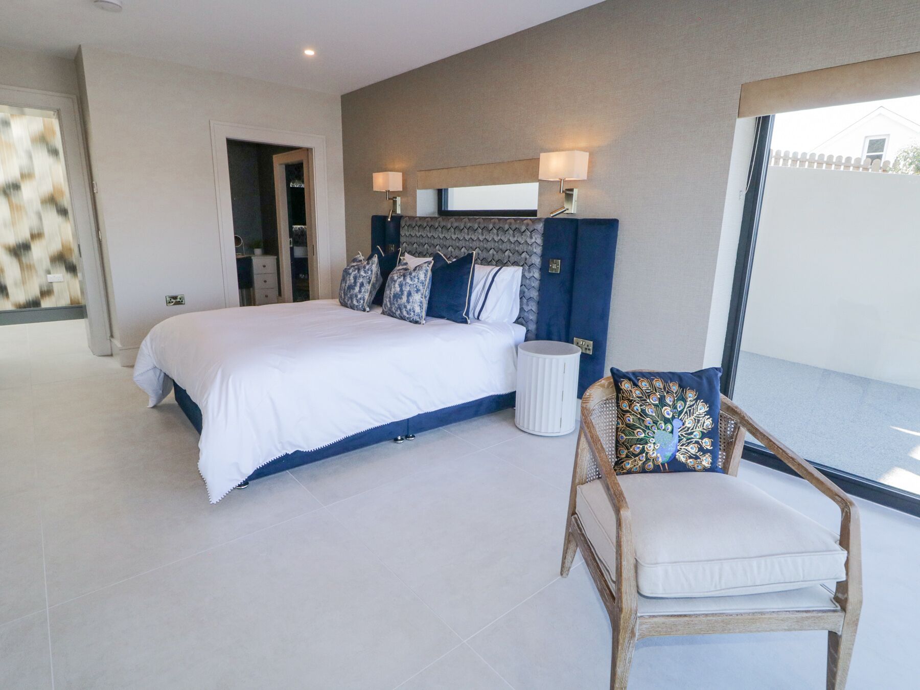 A bedroom with a large bed, a nightstand, a chair, and a window with a view.