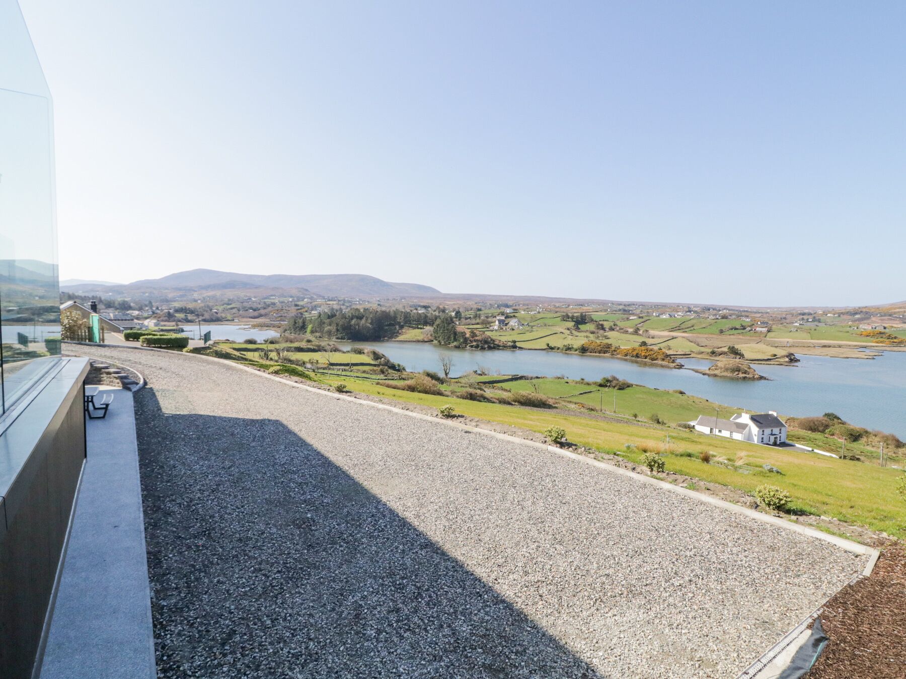 Vista desde una ventana sobre un paisaje rural con un lago, campos y colinas al lejano.