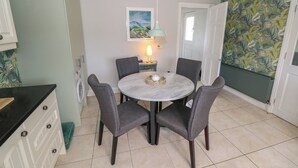 Zona pranzo con un tavolo rotondo, quattro sedie grigie, una lampada a sospensione, un quadro appeso al muro e carta da parati decorata sulla parete adiacente.