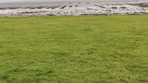 A grassy field with a distant view of a beach and rocky formations. - RIVER VIEW POD, pet friendly, with open fire in Muff, County Donegal (Muff)