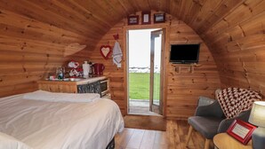 A cozy cabin room with a bed, a small table, a chair, a television, and a door leading outside. - RIVER VIEW POD, pet friendly, with open fire in Muff, County Donegal (Muff)
