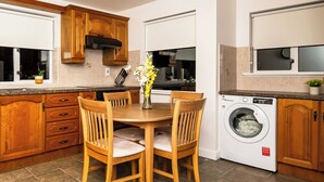 A kitchen with wooden cabinets, a dining table with chairs, a washing machine, and a window with a clock.