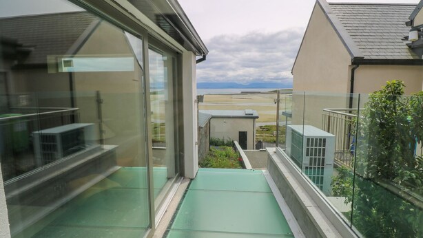Un balcon moderne avec des garde-corps en verre, un plancher en verre vert et une vue sur la mer et les bâtiments au loin.