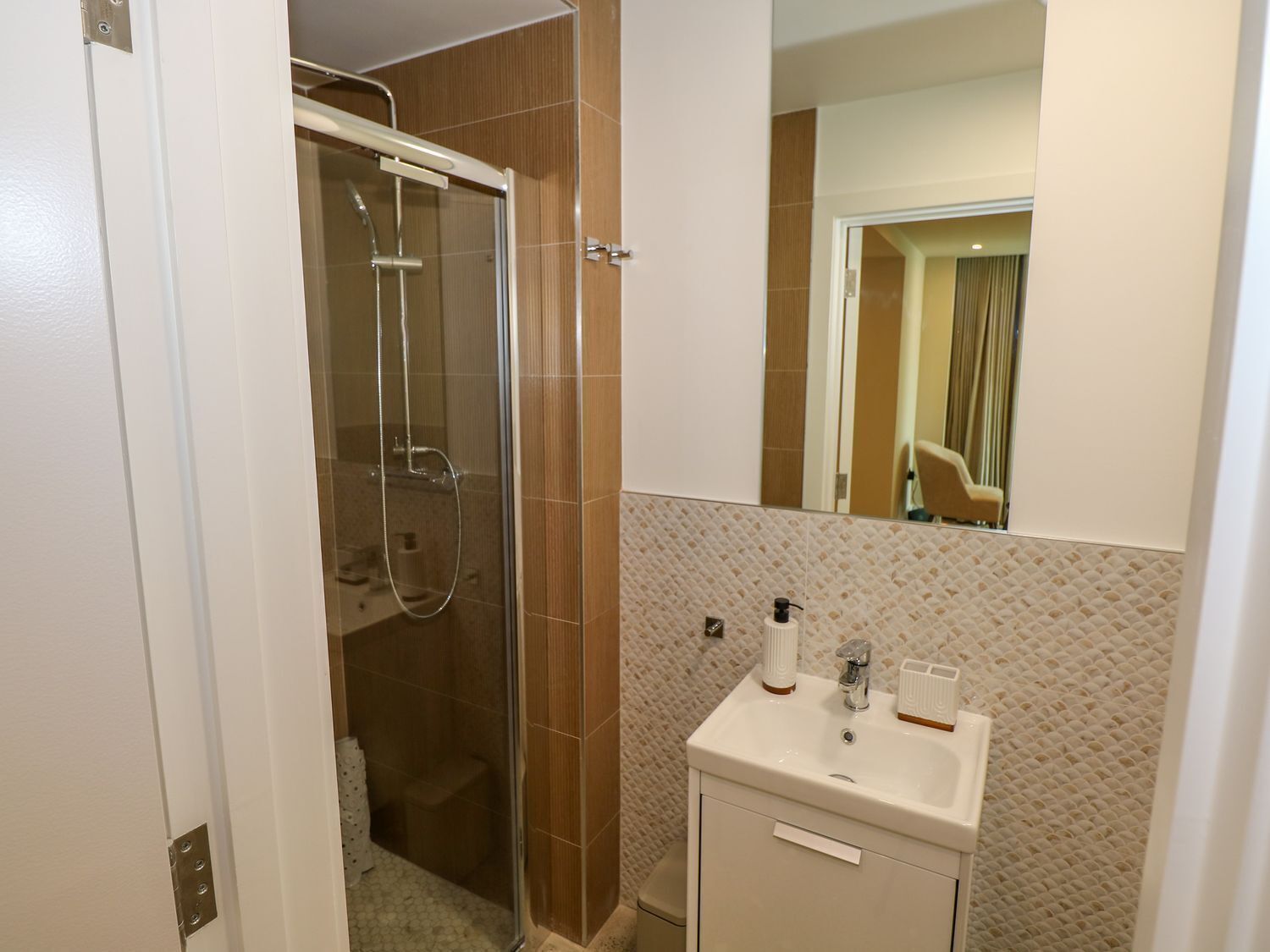 A bathroom with a glass-enclosed shower, a white sink with a mirror, and a tiled wall.