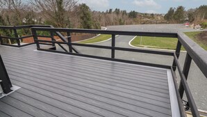 A wooden deck with a railing overlooking a parking area and a road.