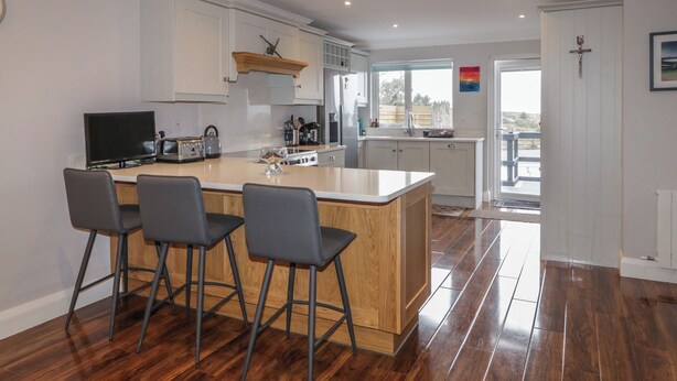 A modern kitchen with a central island, bar stools, and a dining area.