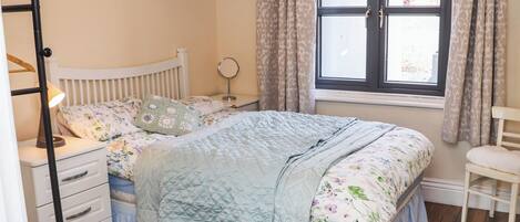 A bedroom with a bed, a nightstand, a dresser, a chair, and a window with curtains.