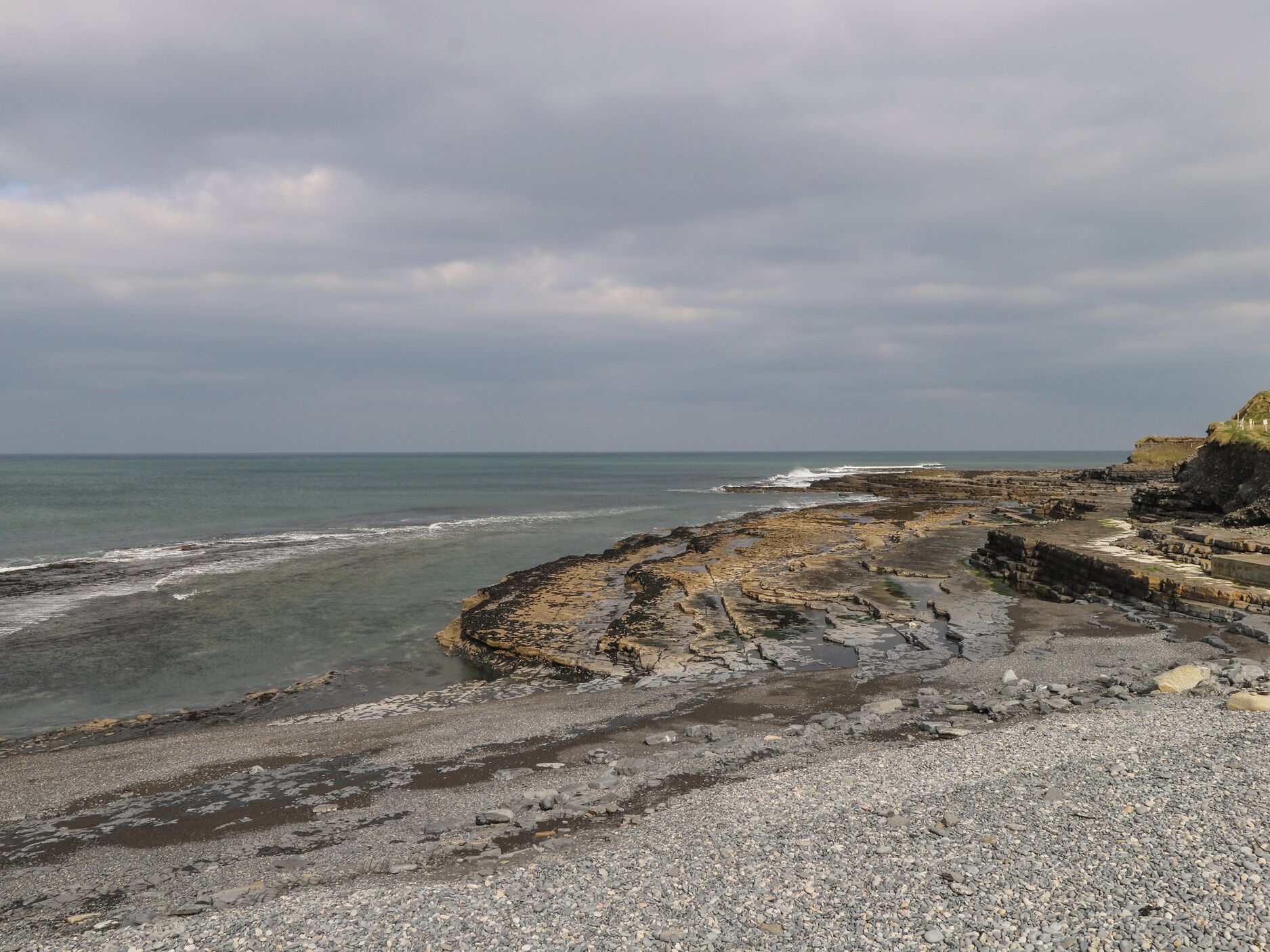 A rocky coastal landscape with a pebbly beach and a cliff.