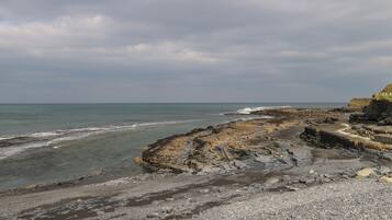 A rocky coastal landscape with a pebbly beach and a cliff.