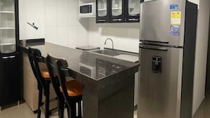 Une cuisine moderne dotée d’un îlot central, de meubles de couleur noire, d’un réfrigérateur en acier inoxydable et d’un four à micro-ondes placé au-dessus des meubles.