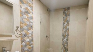 Une salle de bain avec un lavabo, des toilettes et une douche, le tout de couleur blanche. Les murs sont recouverts de carreaux disposés selon un motif géométrique.
