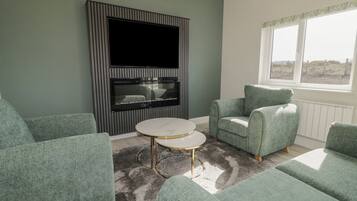 A living room with green upholstered sofas, a round coffee table, and a flat-screen TV mounted on a wall with vertical stripes.