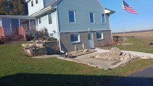 Une maison à deux étages, avec des fondations en pierre, un porche à l’avant et un drapeau américain.
