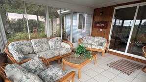 Un patio couvert aménagé avec des meubles en osier, une table en verre et un panneau d’accueil.