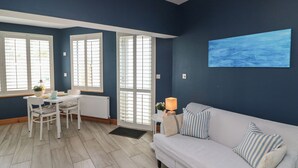 Ein Zimmer mit blauer Wand, einem weißen Sofa, einem Esstisch mit Stühlen und einem Fenster mit Jalousien.