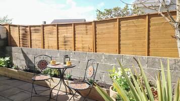 Eine Terrasse mit zwei Metallstühlen, einem kleinen Tisch, einem Holzzaun und Topfpflanzen.