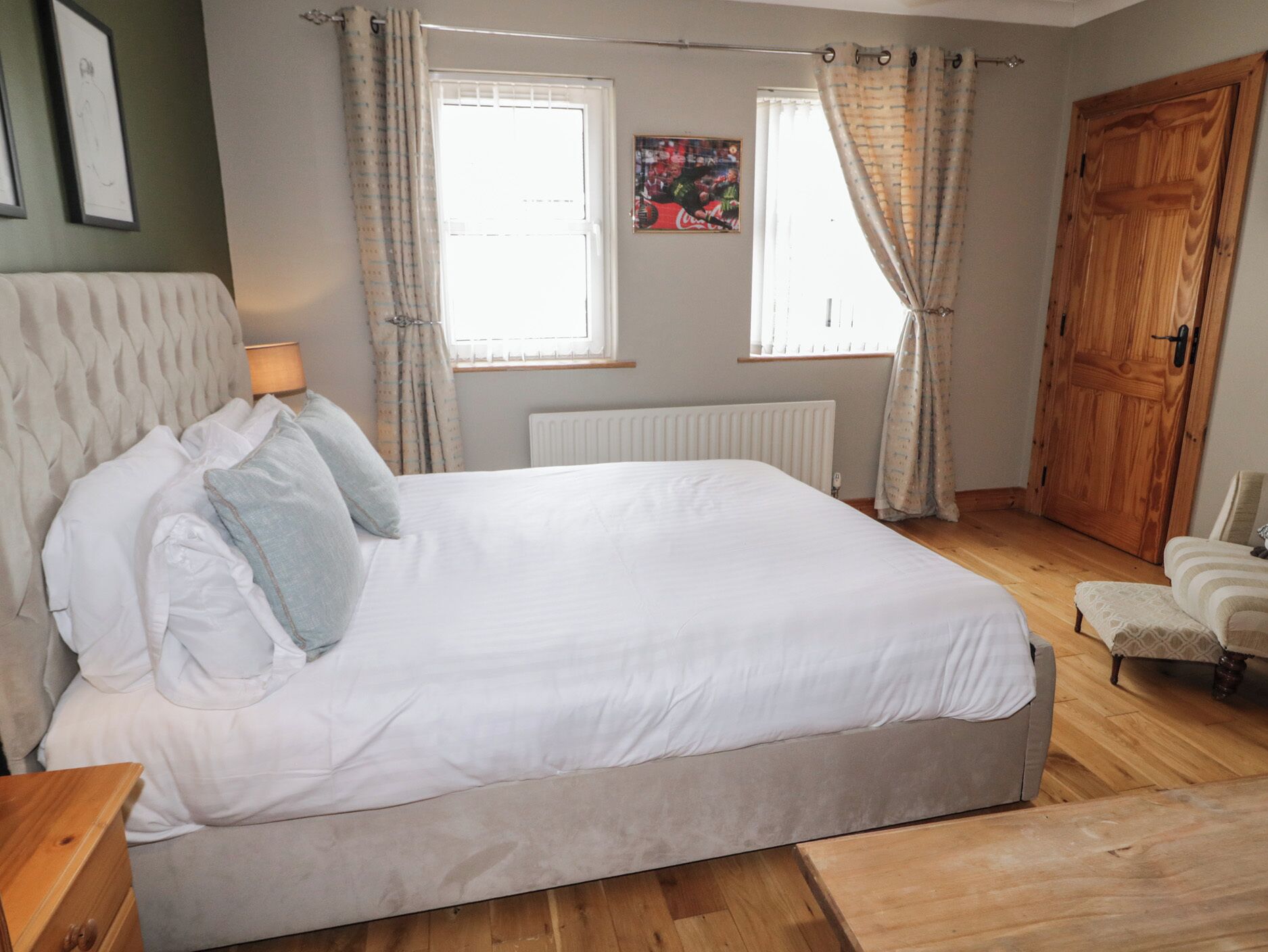 A bedroom with a large bed, a wooden wardrobe, a window with curtains, and a radiator.