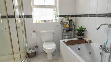 Een badkamer met toilet, badkuip, douche en een douchecabine met glazen wanden.