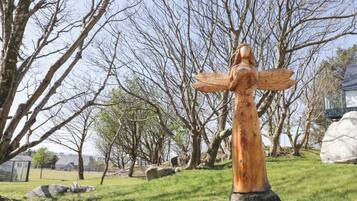 Escultura de fusta d'una dona amb els braços estesos a un parc amb arbres i roques.