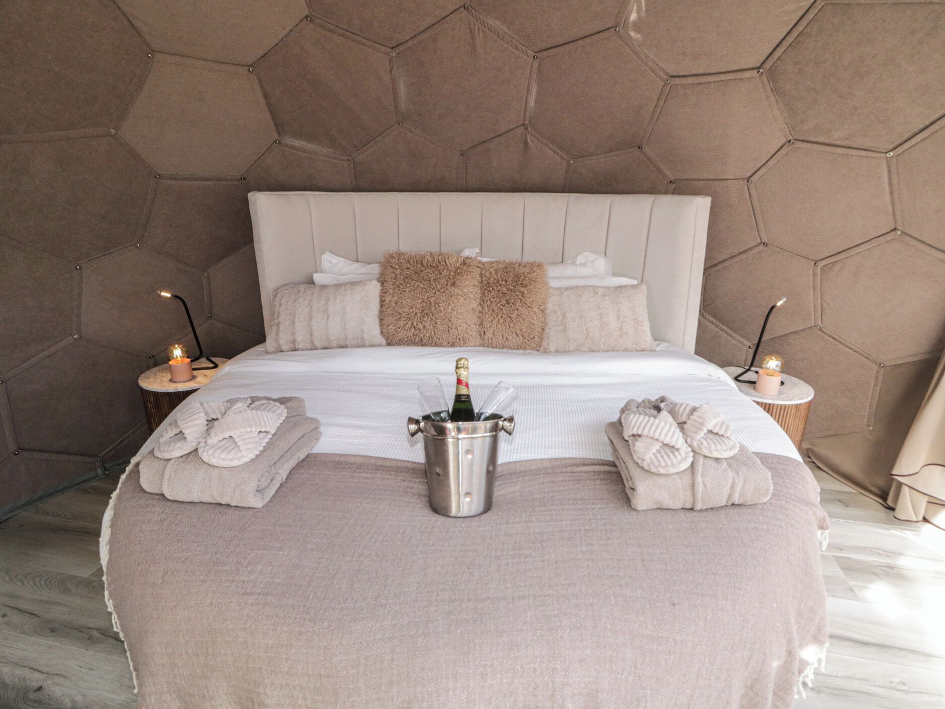 Een slaapkamer met een groot bed, een nachtkastje met een fles champagne en twee handdoeken op het bed.