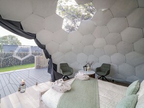 Ein raumiges Zimmer mit sechseckigem Muster, einem Bett, zwei Stühlen, einem kleinen Tisch und Blick ins Freie.