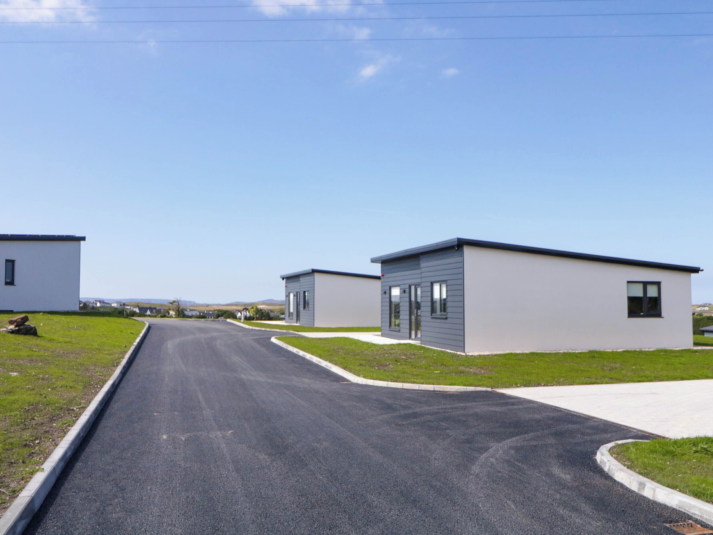 Uma fileira de casas móveis modernas, térreo, com um caminho pavimentado que leva a uma área gramada.