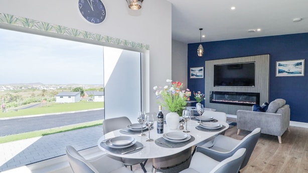 A modern dining area with a large table set for four, a television mounted on the wall, and a view of the outdoors. - NUMBER 5 VILLA - THE VIEW, with a garden in Derrybeg, County Donegal (Derrybeg)