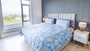 A bedroom with a large bed, a nightstand, a lamp, and a view of the outdoors. - NUMBER 5 VILLA - THE VIEW, with a garden in Derrybeg, County Donegal (Derrybeg)