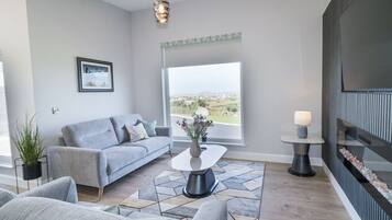 A modern living room with a grey sofa, a coffee table, and a view of the countryside.