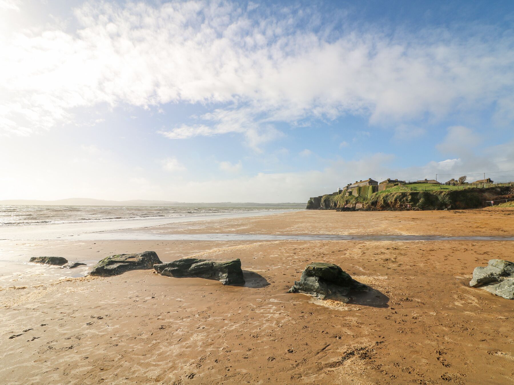 A beach with rocky outcrops and a distant view of a fortified structure on a cliff.
