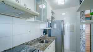 Een moderne keuken met witte tegels, een roestvrijstalen koelkast, een magnetron en een granieten spoelbak.
